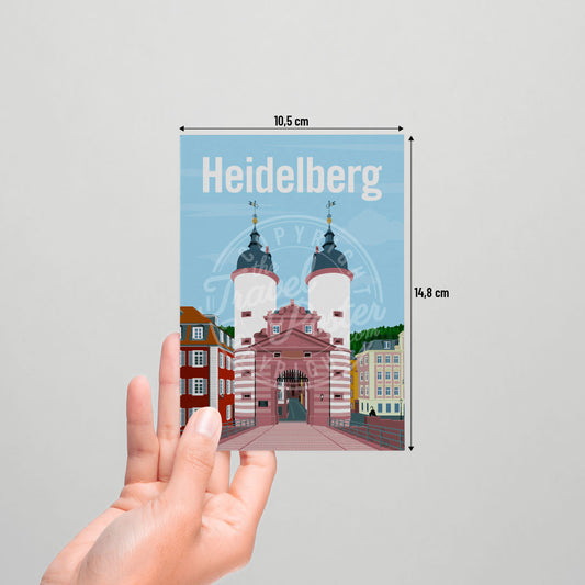 A hand holding a postcard of the Heidelberg Bridge Gate on a white background.