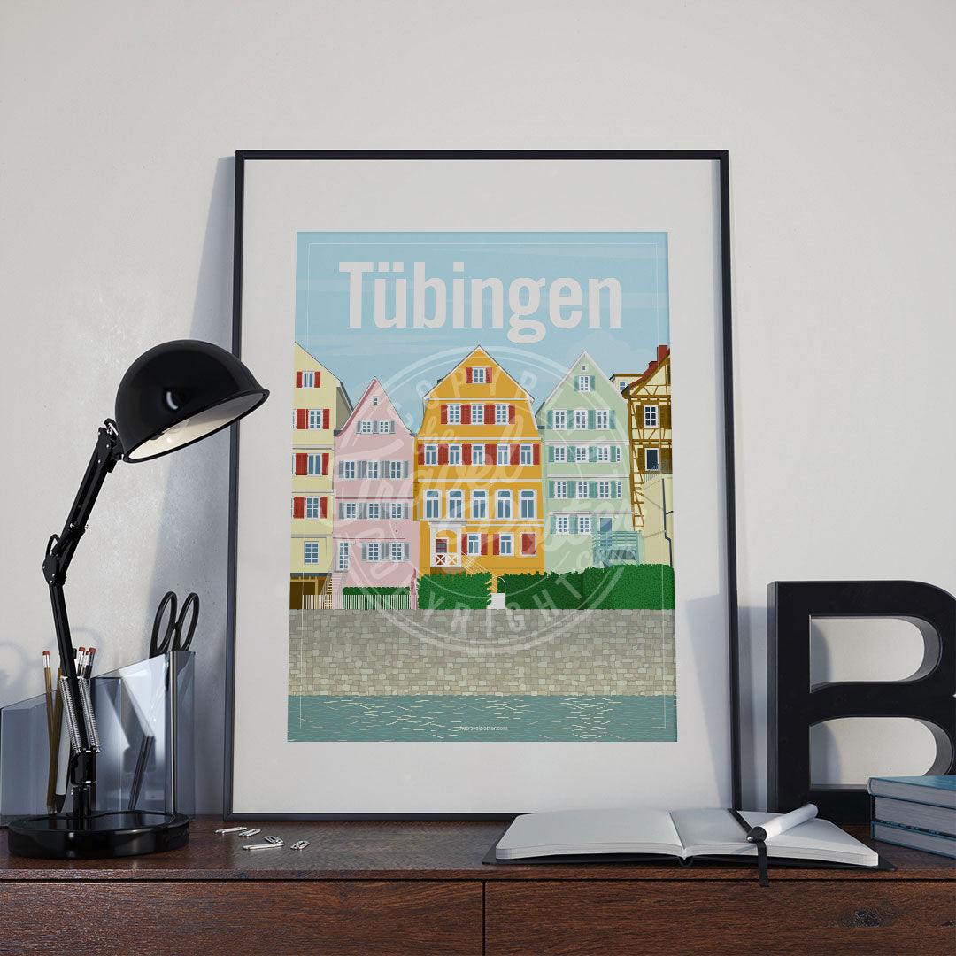 a frame with a poster of the Neckar riverfront in Tübingen, placed a wooden sideboard with a table lamp and stationery supplies