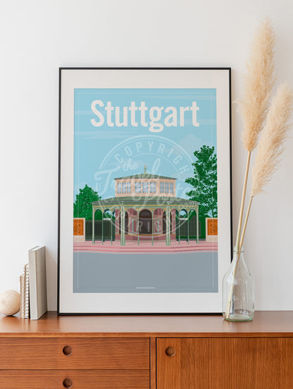 a frame with a poster of the Stuttgart Wilhelma Kassenpavillon, placed on a wooden sideboard with some books and reeds in a glass bottle