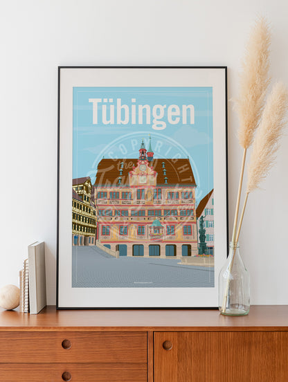 a frame with a poster of the Tübingen Rathaus, placed on a wooden sideboard with some books and reeds in a glass bottle